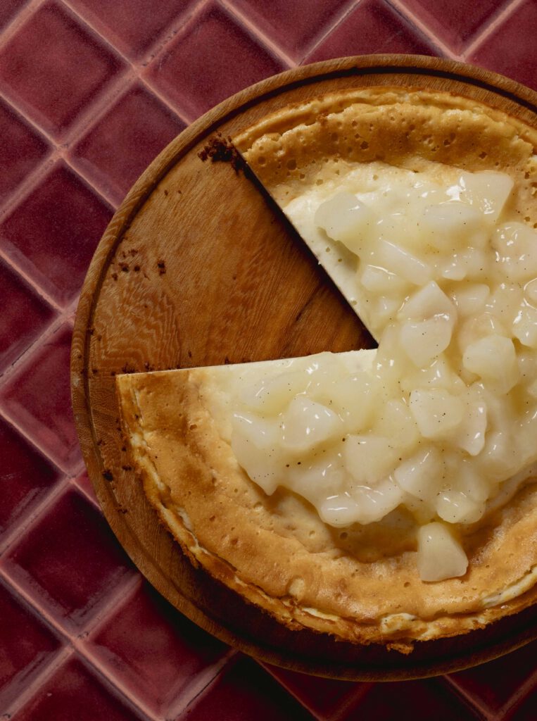 Aufgeschnittener cremiger Käsekuchen mit Vanille und Piment und Birnenkompott auf einer Holzplatte