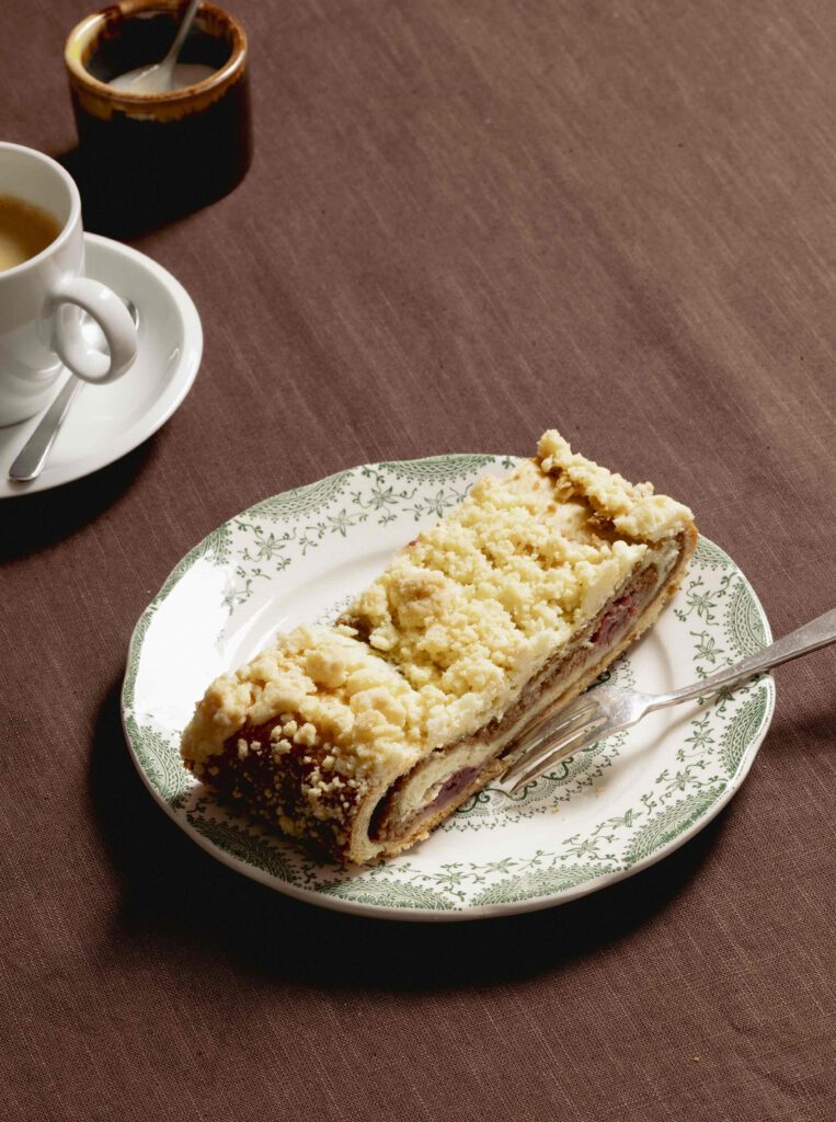 Ein Stück Walnuss-Kirsch-Striezel mit Streuseln, auf einem Teller und Kaffeetasse